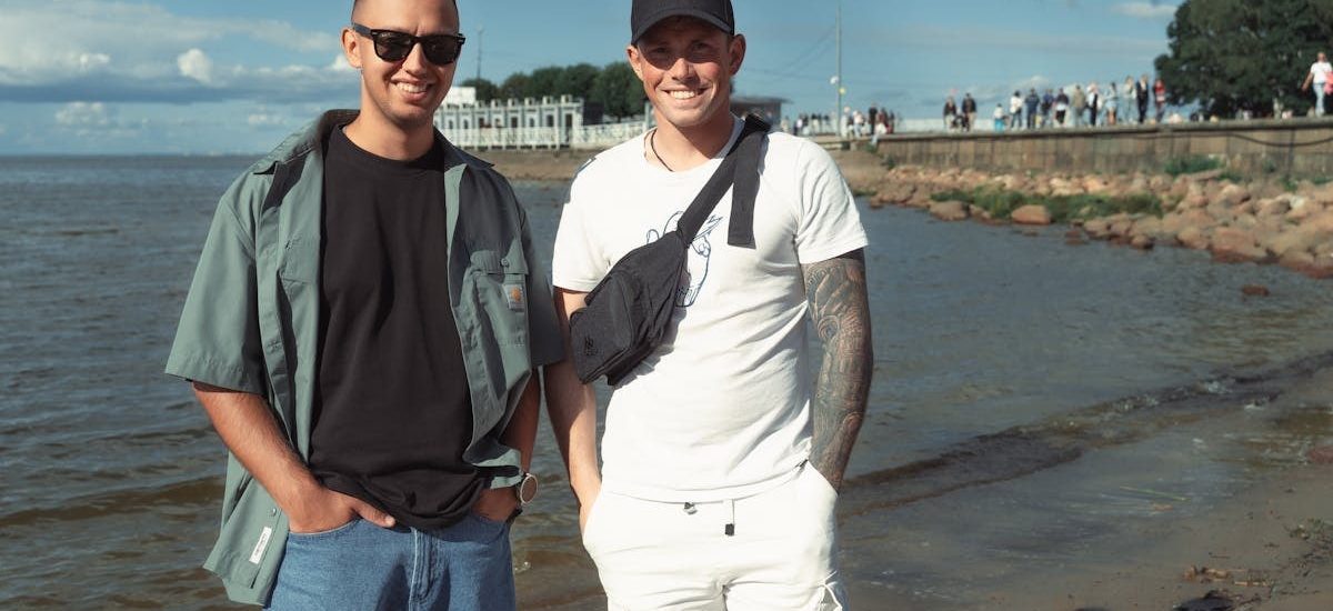 Two young men smiling near the sea on a sunny day, enjoying the beach atmosphere.