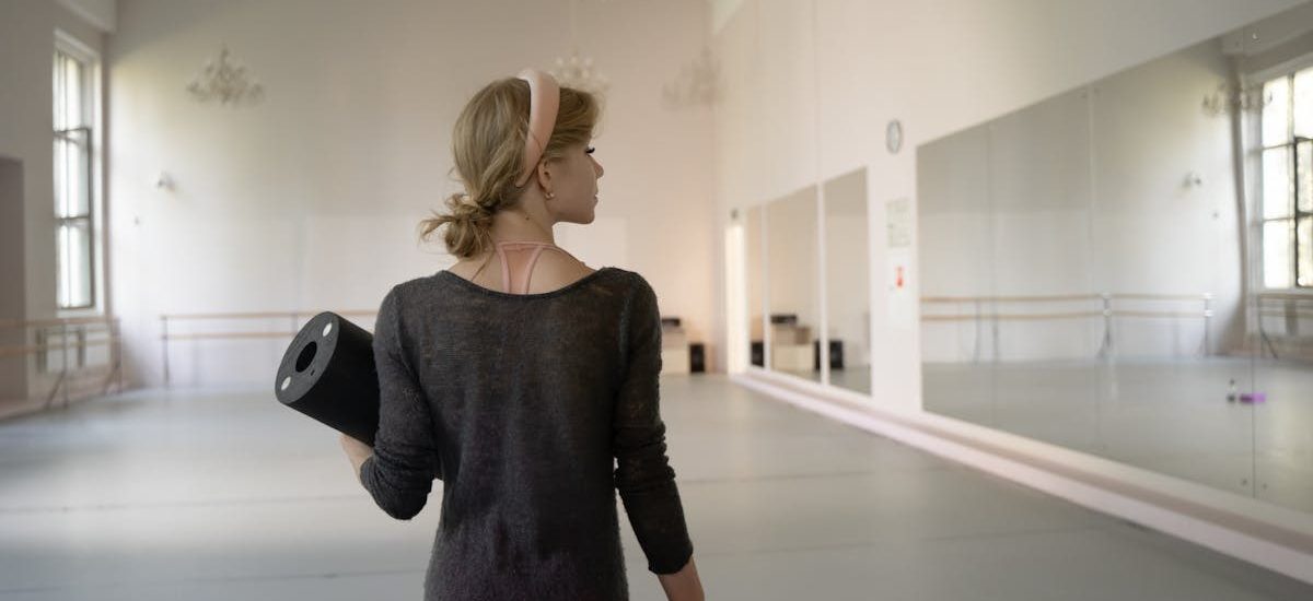 A ballet dancer holds gear in a spacious and elegant studio, ready for practice.